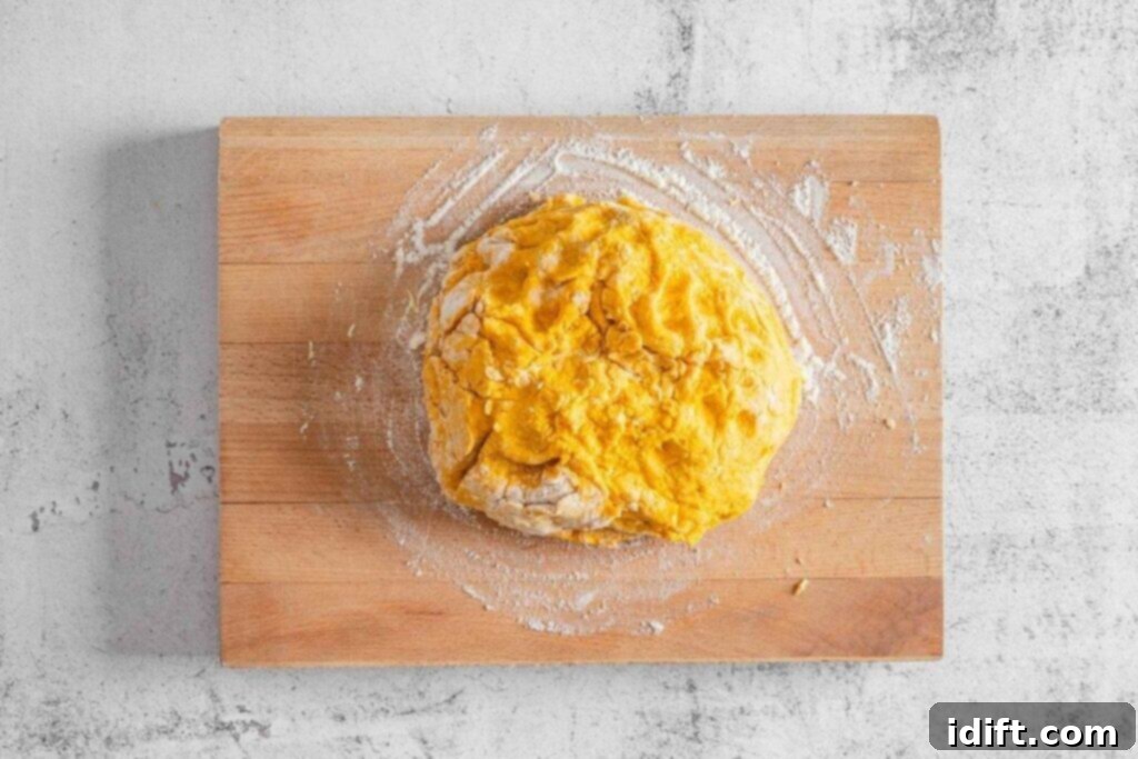 A ball of yellow dough sits on a floured wooden cutting board atop a light gray textured surface.