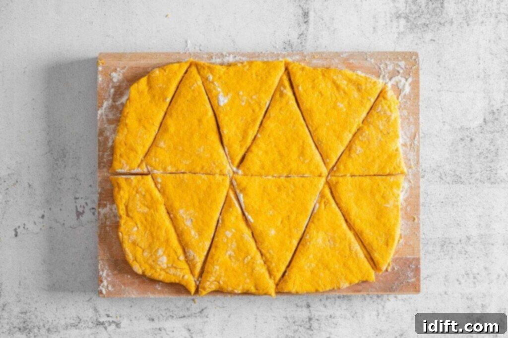Rectangular sheet of orange dough cut into triangle pieces on a floured wooden board, viewed from above.