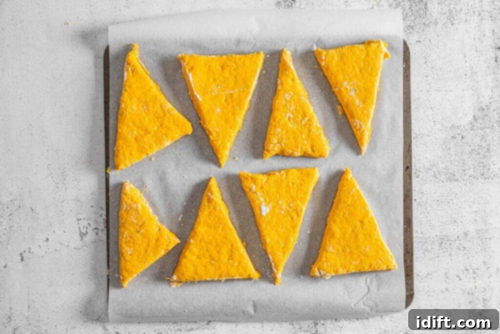 Eight unbaked, triangular orange scones are arranged on a parchment-lined baking tray.