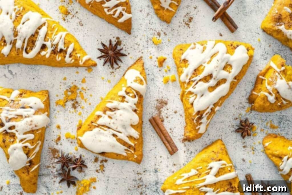 Triangular pumpkin scones topped with white icing are arranged on a light surface, surrounded by cinnamon sticks and star anise.