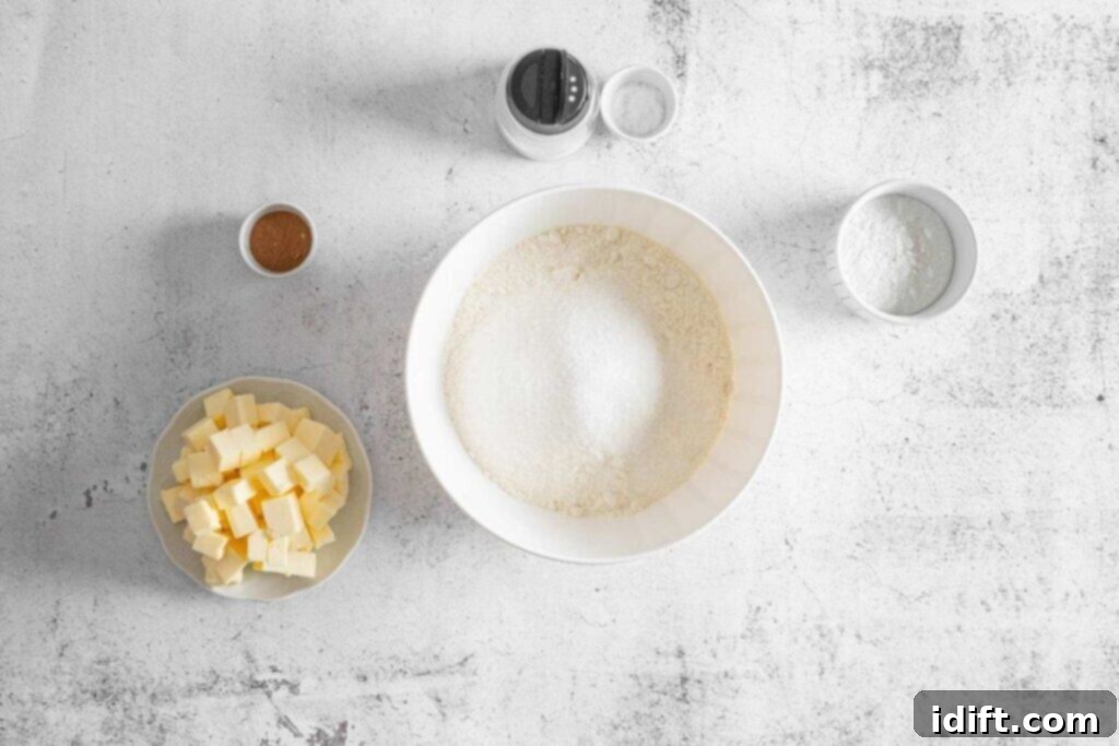 Baking ingredients on a white surface, including a bowl with flour and sugar, a dish of cubed butter, and small bowls of pumpkin pie spice, baking powder, and salt.