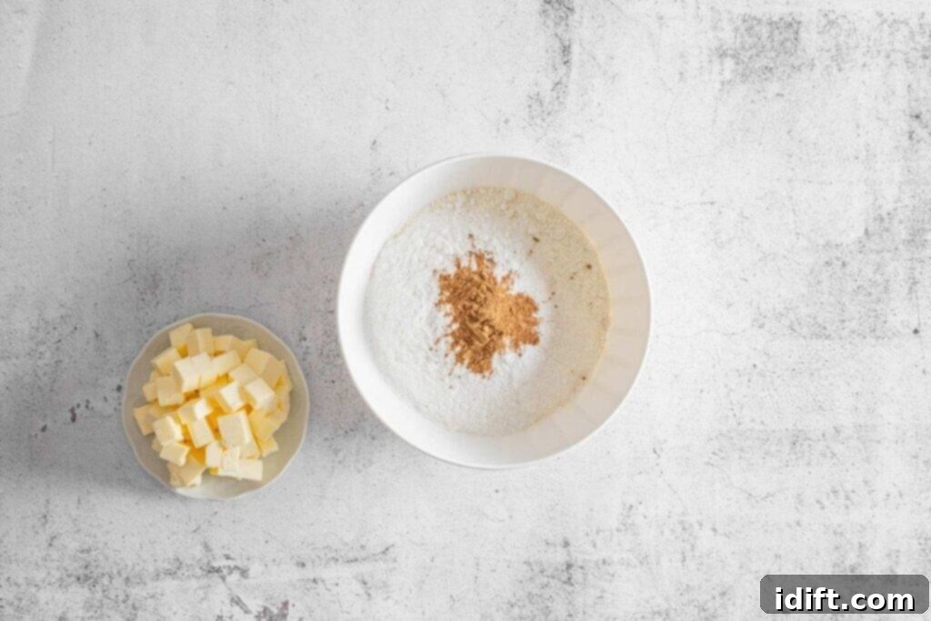 A bowl of cubed butter beside a large bowl containing all the dry ingredients on a light textured surface.