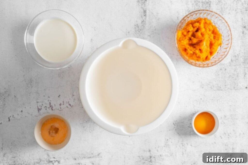 Four bowls containing cream, pureed pumpkin, egg, and vanilla are arranged alongside an empty mixing bowl on a light, textured surface.