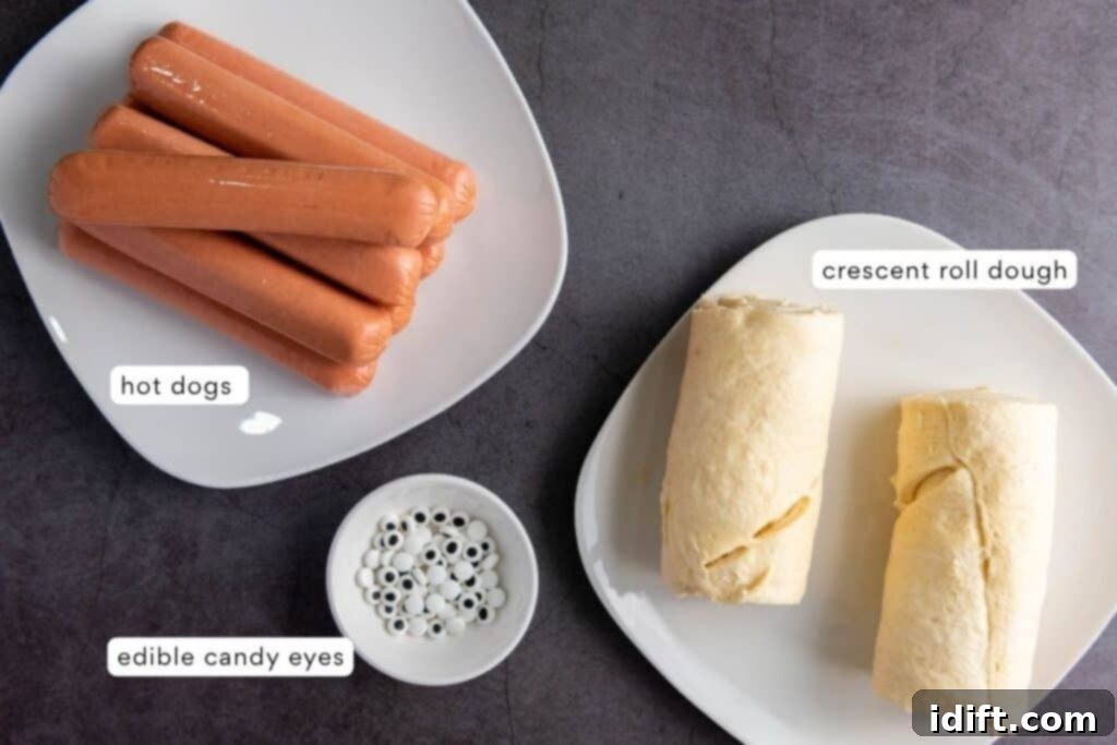 A simple flat lay showing the three main ingredients: a pack of hot dogs, two tubes of crescent roll dough, and a small bowl of edible candy eyes, all neatly arranged on a gray surface with labels.