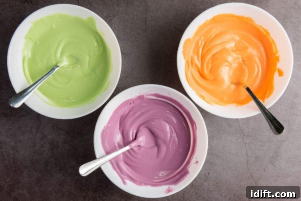 Three glass bowls, each containing vibrant melted candy in green, orange, and purple, with a spoon resting in each, all arranged on a dark countertop.