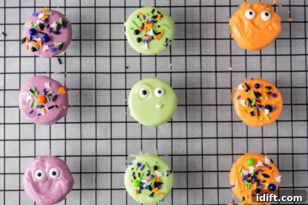 A grid of nine vibrantly colored, round cookies, each intricately adorned with candy eyes and sprinkles, resting on a black cooling rack.