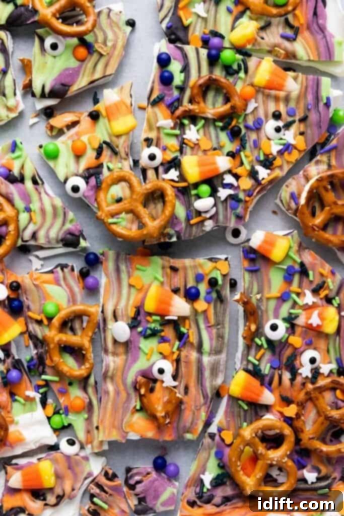 Colorful Halloween bark topped with candy corn, pretzels, candy eyes, sprinkles, and chocolate, broken into pieces on a flat surface.
