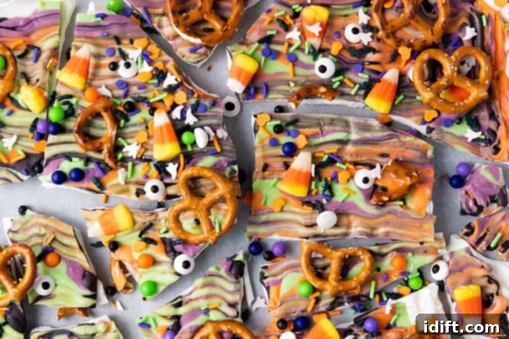 Halloween-themed chocolate bark topped with pretzels, candy corn, candy eyeballs, and colorful sprinkles, broken into irregular pieces.