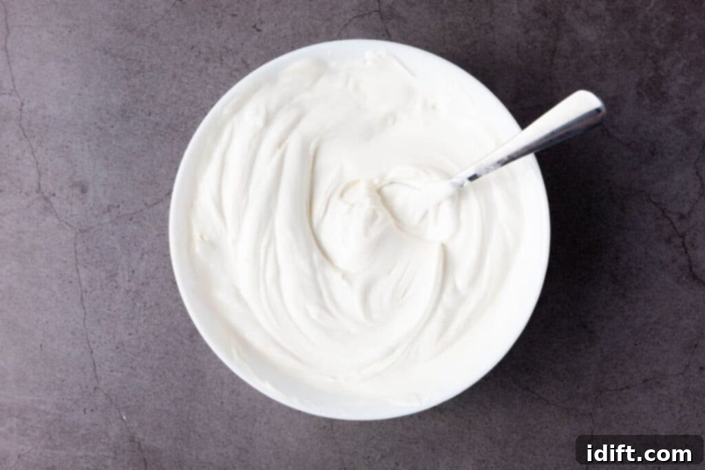 A white bowl filled with melted white candy with a metal spoon resting inside, placed on a gray textured surface.