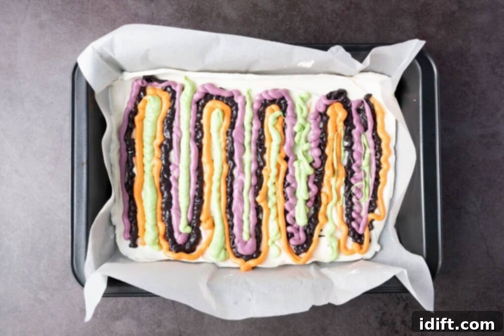 A rectangular baking pan lined with parchment paper holds a dessert topped with wavy lines of orange, purple, green, and black glaze.