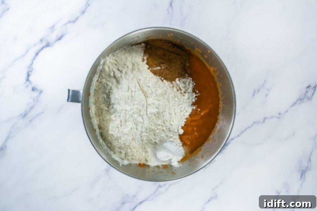 Mixing bowl with pumpkin batter ingredients, including flour, salt, baking soda, baking powder, and pumpkin pie spice before blending.