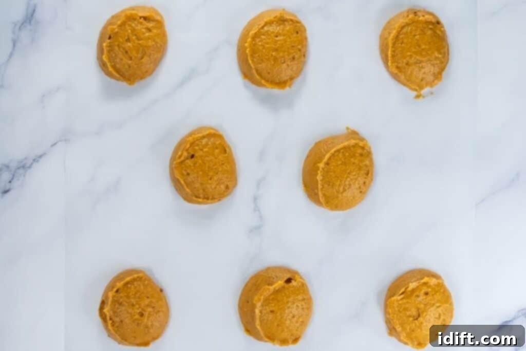 Raw pumpkin whoopie pie batter scooped into rounds on parchment paper, ready for baking.