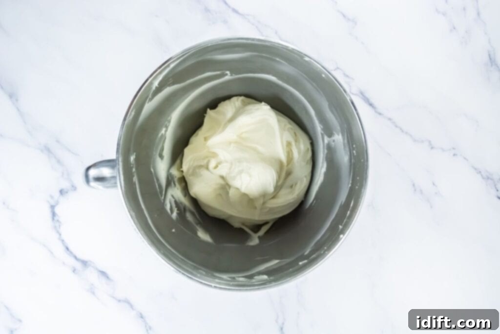 Bowl of smooth cream cheese frosting in a metal mixing bowl on a marble surface.