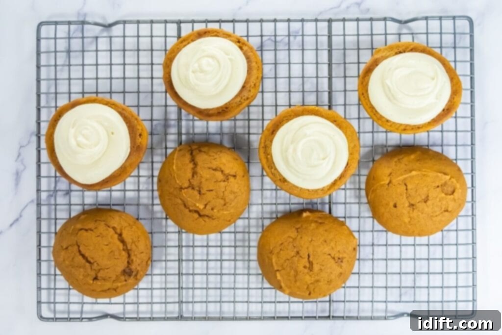 Pumpkin whoopie pie halves on a cooling rack, some topped with cream filling and others plain.
