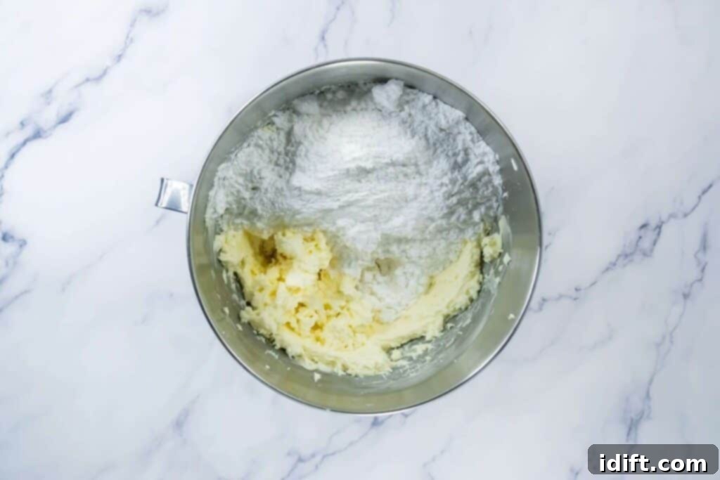 Adding flour mixture to creamed butter and sugar in a bowl on a marble counter.