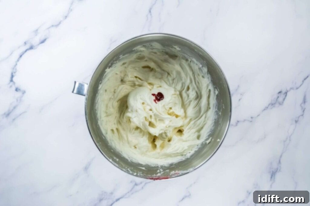 Light pink cream cheese frosting in a mixing bowl on a marble counter.