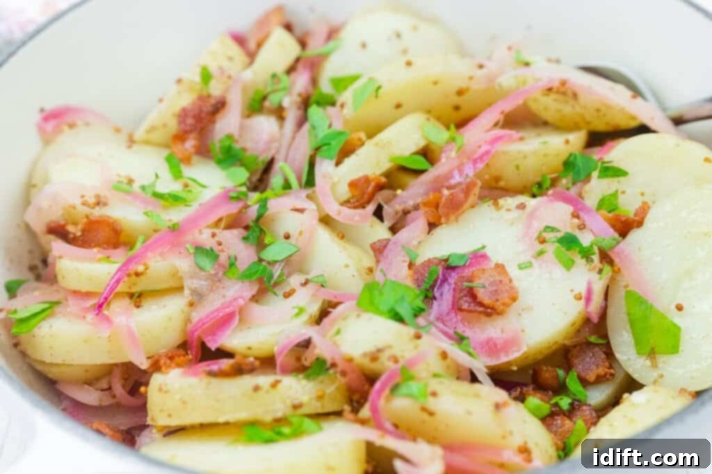 A bowl of sliced potatoes mixed with bacon, red onions, chopped parsley, and a grainy mustard dressing.