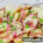 A white dish filled with sliced potatoes, red onions, bacon bits, and chopped parsley, with a serving spoon on the side.