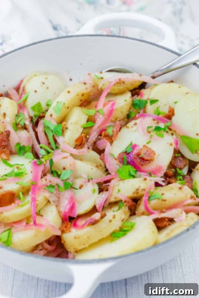 A white dish filled with sliced potatoes, red onions, bacon bits, and chopped parsley, with a serving spoon on the side.