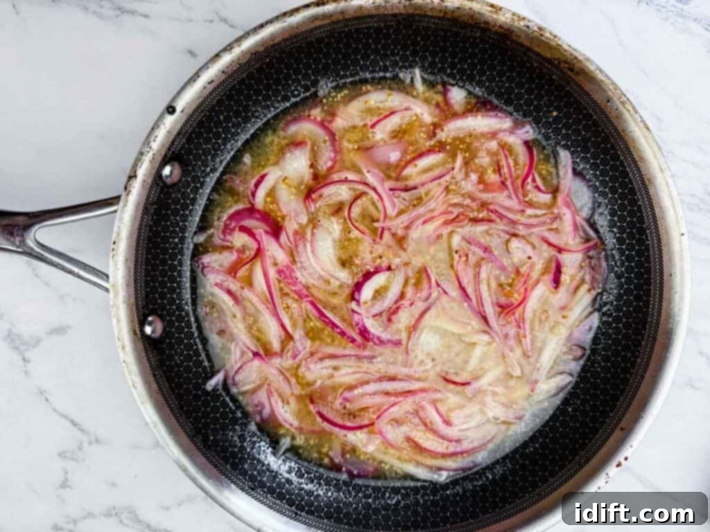 A frying pan on a marble surface containing sliced red onions cooking in oil or liquid.