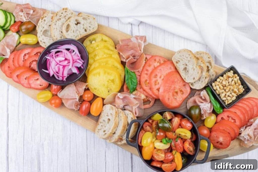 Tomato Flight Selection 2 A wooden board with assorted sliced bread, prosciutto, yellow and red tomatoes, pickled onions, cherry tomatoes, pine nuts, and a bowl of tomato salad on a white surface.