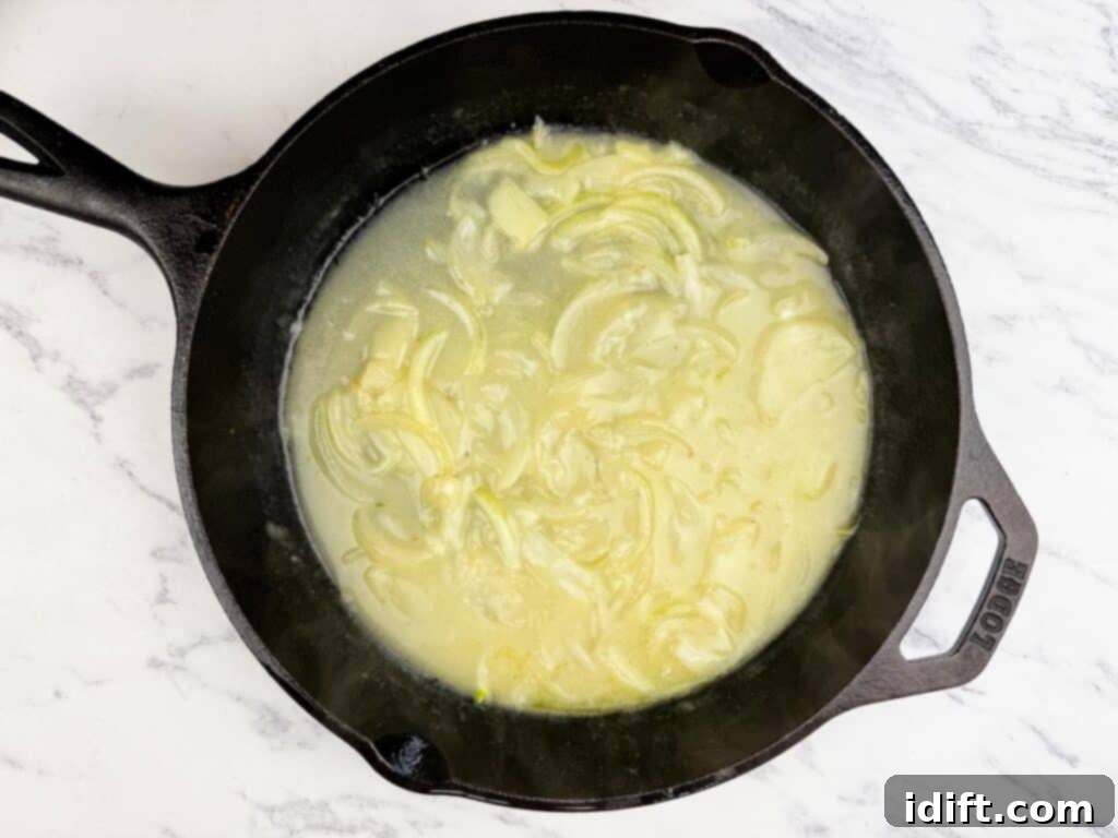 Sliced onions cooking in a creamy sauce inside a black cast iron skillet on a white marble countertop.