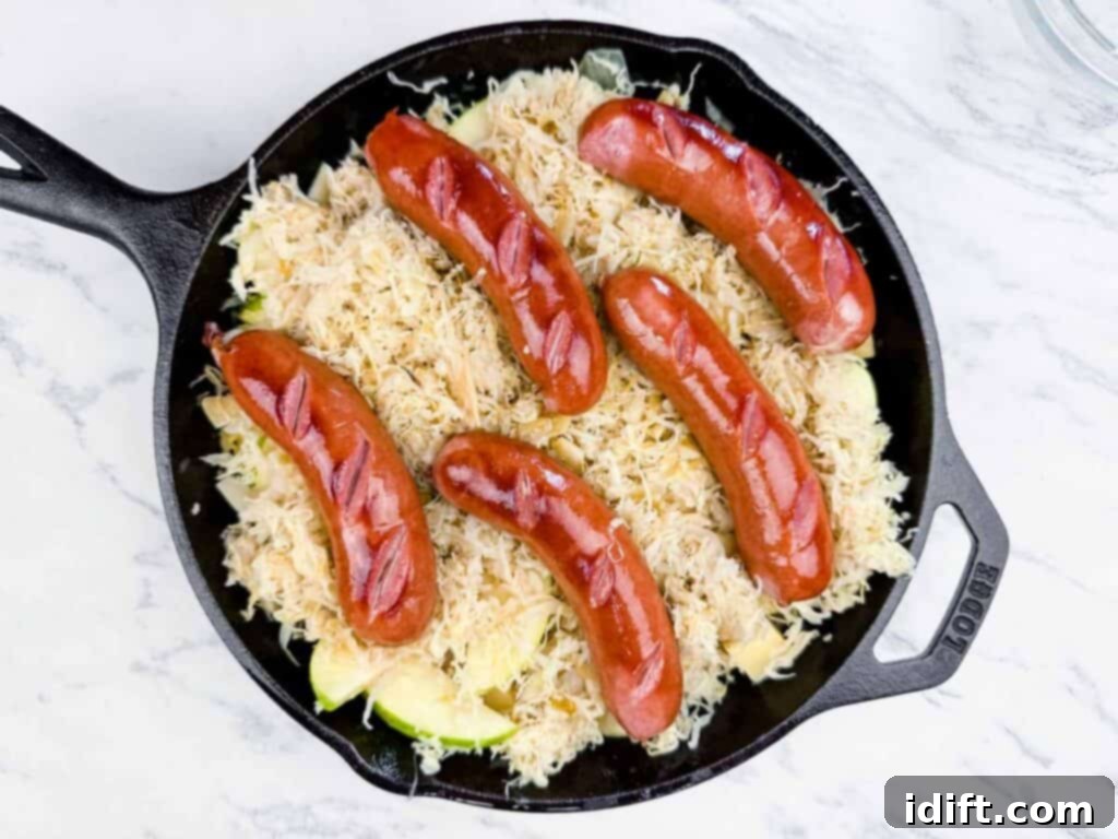 A cast iron skillet containing sliced sausage links arranged on top of a layer of sauerkraut and chopped vegetables.