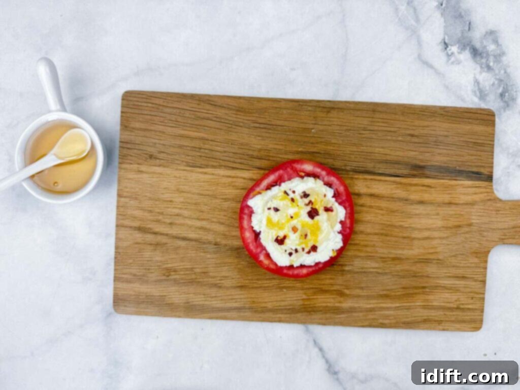 A gourmet close-up of a fresh tomato slice artfully topped with creamy cottage cheese and a delicate blend of seasonings, resting on a rustic wooden cutting board. Nearby, a small elegant cup of golden honey with a matching spoon awaits on a sleek marble surface, enhancing the visual appeal.