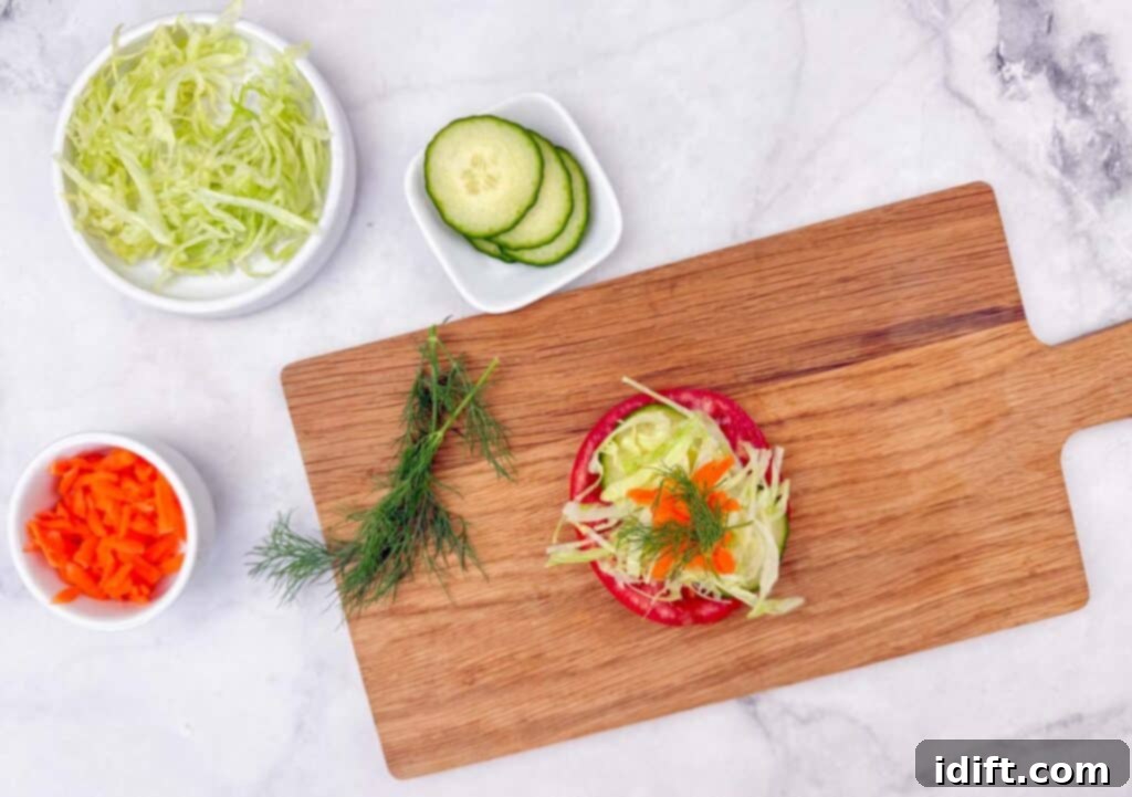 A rustic wooden cutting board features a vibrant tomato slice beautifully adorned with shredded lettuce, delicate cucumber slices, and fresh dill. Surrounding the board are elegant bowls containing additional shredded lettuce, thinly sliced cucumber, and precisely diced orange bell pepper, creating a visually appealing and fresh culinary display.