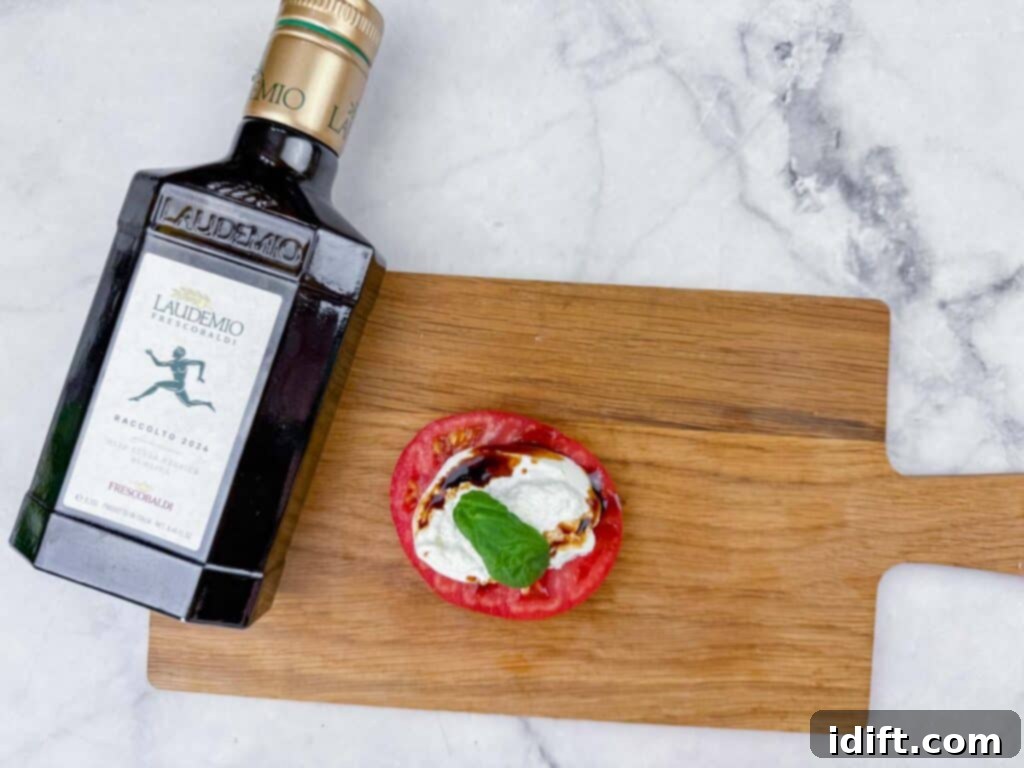 A bottle of premium Laudemio olive oil sits on a rustic wooden board, next to a perfectly sliced tomato adorned with creamy burrata cheese, fresh basil, and a luscious balsamic glaze, embodying gourmet freshness.