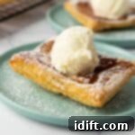 A square piece of puff pastry topped with a scoop of vanilla ice cream and dusted with powdered sugar on a light blue plate.