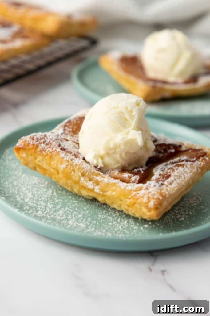 A square piece of puff pastry topped with a scoop of vanilla ice cream and dusted with powdered sugar on a light blue plate.