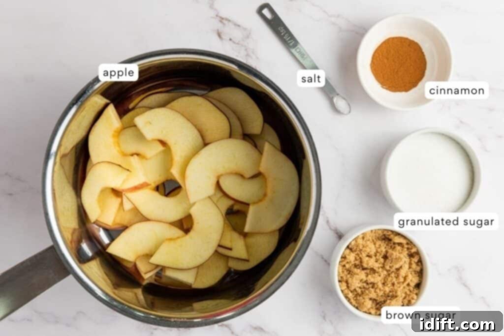 A saucepan with sliced apples next to measured bowls of cinnamon, granulated sugar, brown sugar, and a measuring spoon of salt on a marble surface.