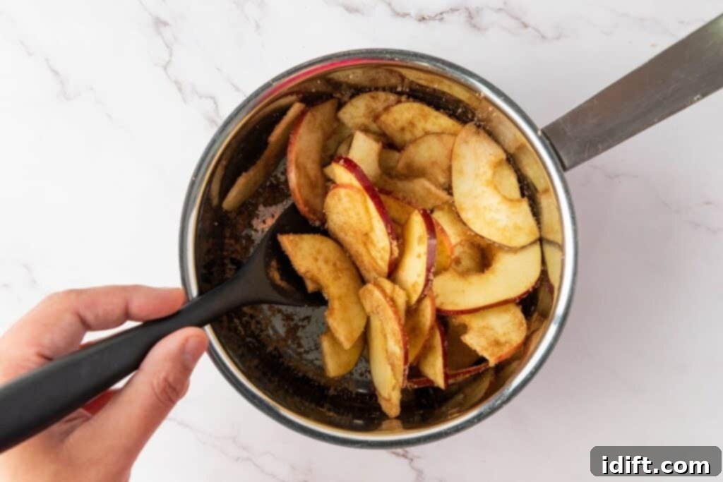Sliced apples coated with cinnamon and sugar being stirred in a saucepan with a black spoon.