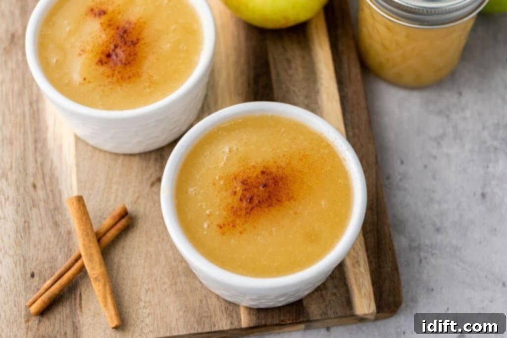 Chef Jenn's Effortless Instant Pot Applesauce 3 Two small white bowls of applesauce topped with cinnamon sit on a wooden board next to cinnamon sticks, an apple, and a jar of applesauce.