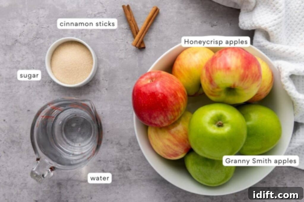 Chef Jenn's Effortless Instant Pot Applesauce 4 A bowl with Honeycrisp and Granny Smith apples, a small bowl of sugar, a measuring cup of water, and two cinnamon sticks on a gray surface.