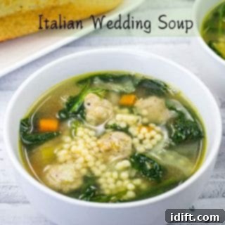 A bowl of Italian wedding soup with meatballs, pasta, spinach, and carrots. A slice of bread is visible in the background.