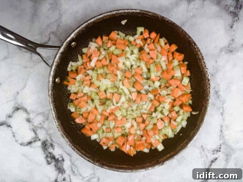 Pan with diced carrots, celery, and onions sautéing on a marble countertop.