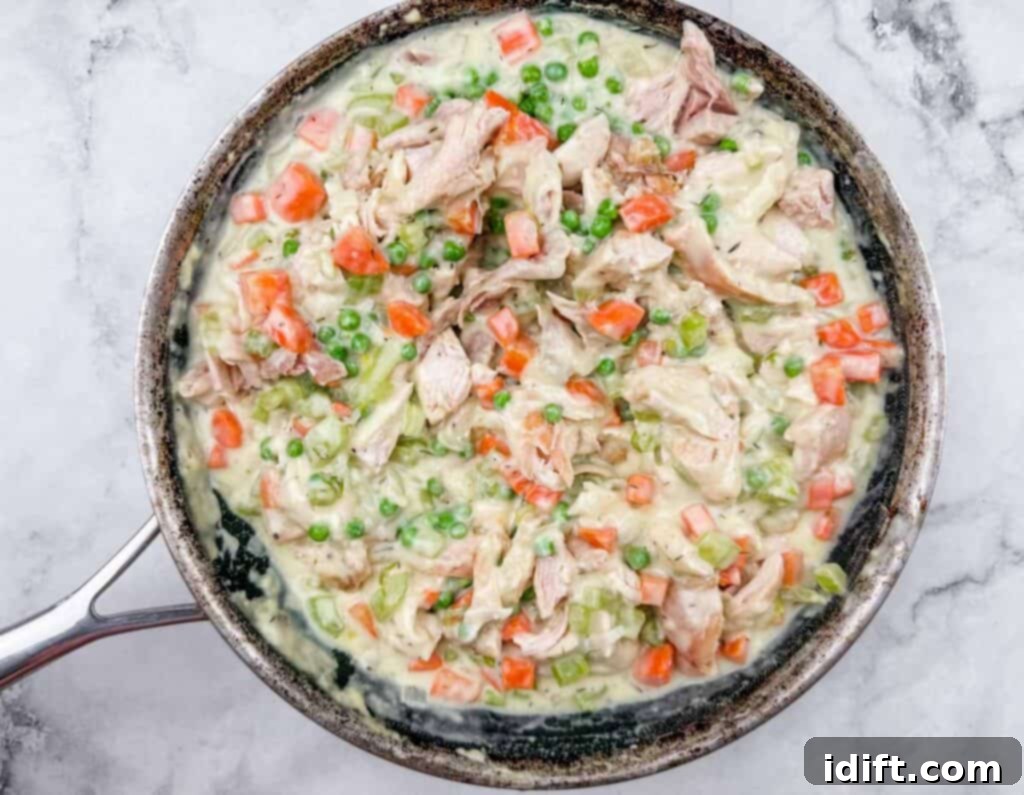 A skillet filled with creamy chicken, peas, carrots, and celery mixture on a marble surface.