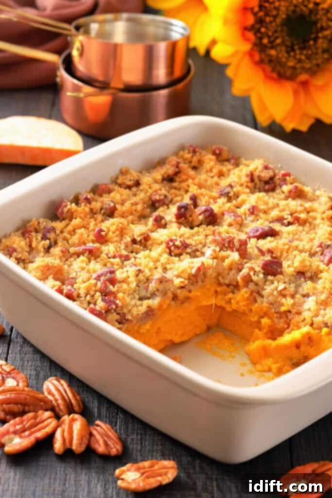 Decadent Sweet Potato Casserole with Crunchy Pecan Streusel 2 A white baking dish with sweet potato casserole topped with pecan crumble, a corner serving missing, pecans scattered, and measuring cups and a sunflower in the background.