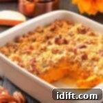 Decadent Sweet Potato Casserole with Crunchy Pecan Streusel 9 A white baking dish with sweet potato casserole topped with pecan crumble, a corner serving missing, pecans scattered, and measuring cups and a sunflower in the background.