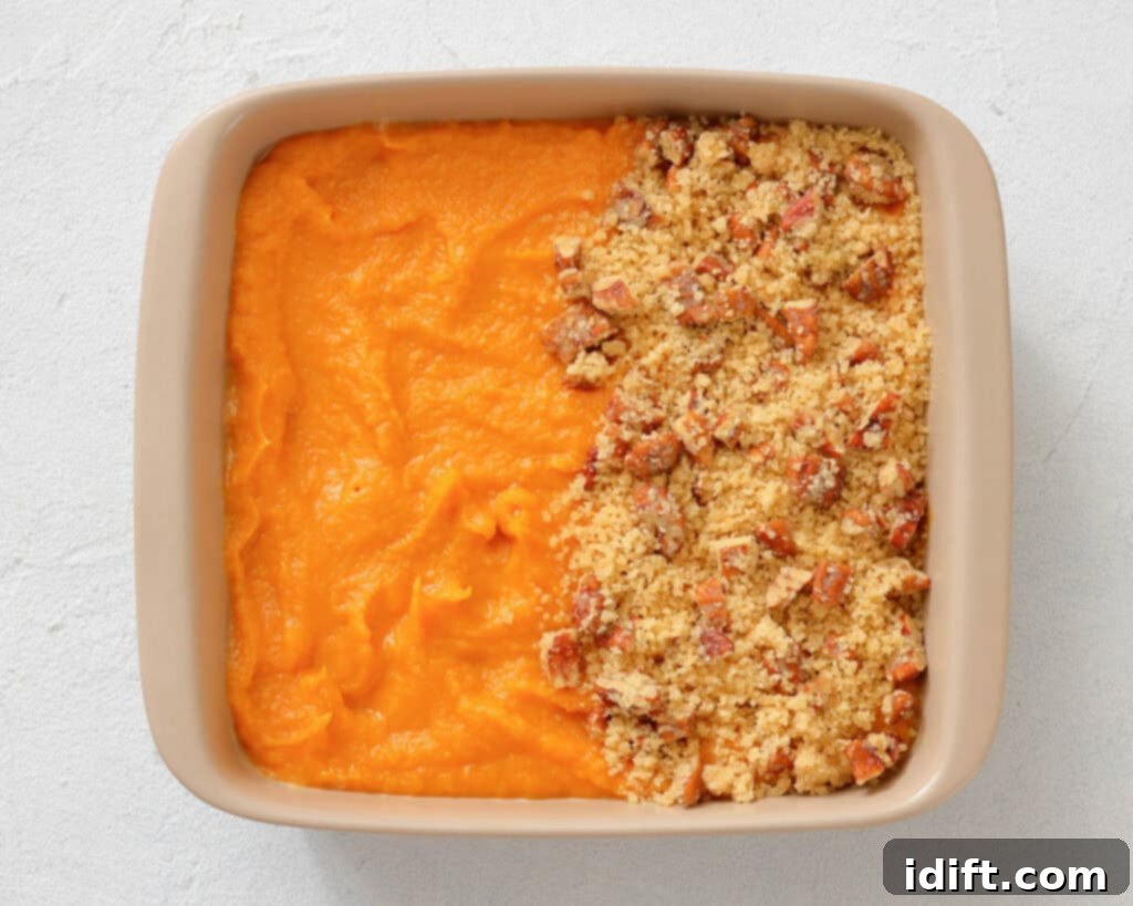 Decadent Sweet Potato Casserole with Crunchy Pecan Streusel 7 Square baking dish with half covered in smooth orange sweet potato puree and the other half topped with a crumbly pecan streusel topping.