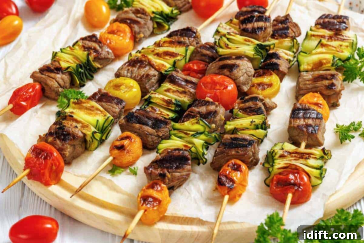 21 Spring-Inspired Dishes to Reinvent Your Week 4 A wooden round serving board is covered with white parchment paper, displaying numerous grilled steak and veggie skewers arranged horizontally across it.